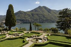 an outdoor seating area in the middle of a garden with water and mountains in the background