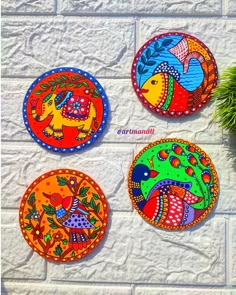 four colorful painted plates sitting on top of a white brick wall next to a potted plant