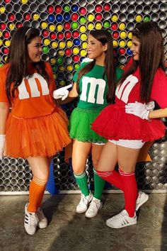 three women dressed up in costumes posing for a photo with colorful balls on the wall behind them