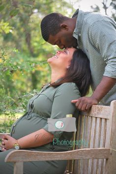 a pregnant woman sitting on top of a wooden bench next to a man who is kissing her belly