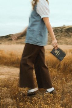 a woman walking across a dry grass covered field