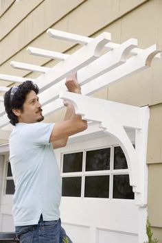 a man is working on a white trellis in front of a house with windows