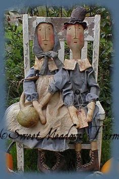 two scarecrows sitting on a chair with pumpkins in the grass behind them