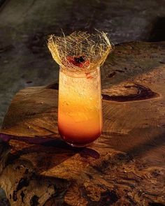 a glass filled with orange liquid sitting on top of a wooden table next to a piece of wood