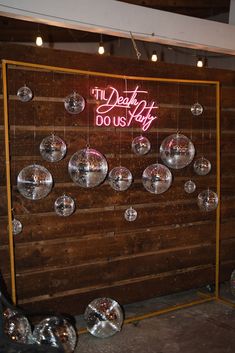 a wooden wall with disco balls hanging from it and a neon sign that reads the dead city do us pay