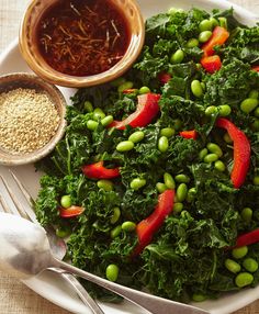 a white plate topped with greens and red peppers next to a bowl of seasoning