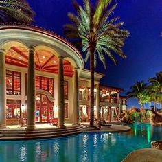 a large house with a pool and palm trees in front of it at night time