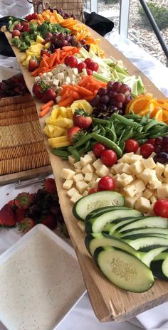 an assortment of fruits and vegetables laid out on a long wooden table in front of a window