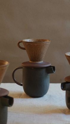 three coffee cups sitting next to each other on top of a white cloth covered table