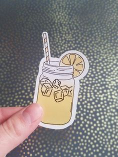 a hand holding up a sticker with a drink in the jar and ice cubes on it