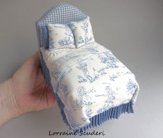 a hand is holding a doll bed with blue and white fabric on it, which has an attached pillow