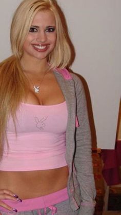 a woman with long blonde hair wearing pink and grey clothing posing for the camera in front of a white wall