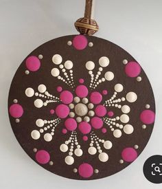 a round ornament with pink and white dots on it hanging from a rope