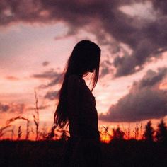 a woman standing in front of a sunset with her head turned to the side and hair blowing back