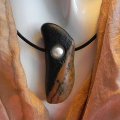 This unique bi-coloured rock makes the perfect frame for a small sweet water pearl. 1.5 mm black leather cord with stainless steel lobster claw closure. Cord length: 48 cm Pendant height: 4.5 cm Pendant width: 1.7 cm Total weight: 15 g Cairn Necklace, Pebble Necklace, Water Pearls, Leather Cord, Hippie Boho, Natural Stones, Black Leather, Jewelry Necklace Pendant, Handmade Items