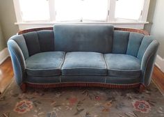 a blue couch sitting on top of a wooden floor next to a window with white curtains