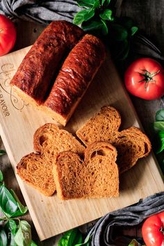 two loaves of bread on a cutting board with tomatoes and basil around it,