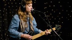 a woman singing into a microphone and playing an electric guitar in front of a microphone with headphones on