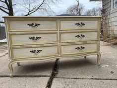 a white and gold dresser sitting on top of a sidewalk in front of a house