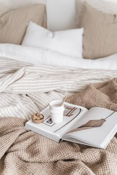 an open book, coffee cup and spoon on a bed with beige linens in the background