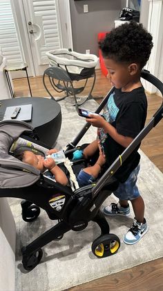 a young boy sitting in a stroller looking at his cell phone while playing with the baby