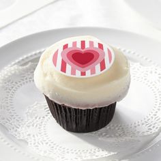 a cupcake on a plate with a heart sticker in the middle, sitting on a lace doily