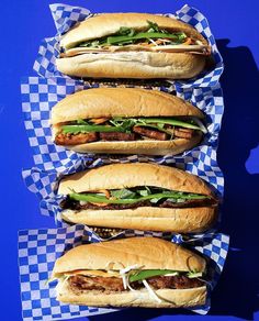 three sub sandwiches sitting on top of blue and white checkered paper with green onions