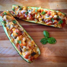 two zucchini boats on a wooden cutting board with basil leaves and cheese in the middle