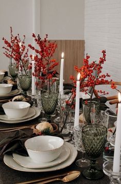 the table is set with white dishes and silverware, candles, and red berries