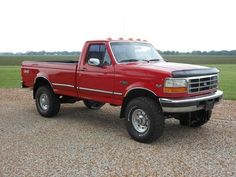 a red pick up truck parked on top of a gravel road next to a field