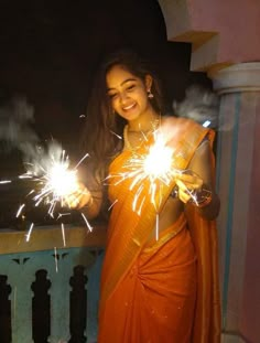 a woman in an orange sari holding sparklers