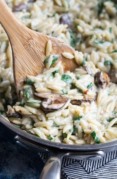 pasta with mushrooms and spinach is being stirred by a wooden spoon in a skillet