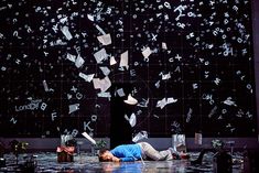 two people laying on the ground in front of a wall with letters falling from it