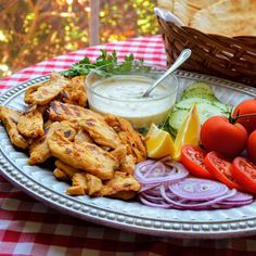 a plate with chicken, tomatoes, onions, cucumbers and pita bread