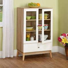 a white and wood cabinet with glass doors on the bottom, in front of a green wall