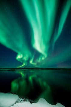 the aurora bore is shining brightly in the night sky over water and snow covered ground