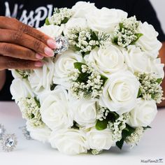 a person holding a bouquet of white roses with a diamond ring on it's finger