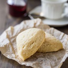 two scones sitting on top of a piece of wax paper next to a cup and saucer