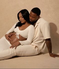 a man and woman are sitting on the floor together, one is holding her belly