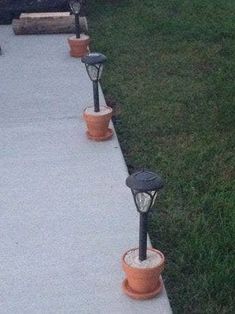 some lights that are sitting on the side of a sidewalk in front of grass and trees