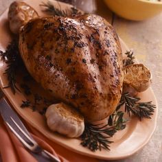 a roasted chicken on a plate with garlic and lemons, next to a knife and fork