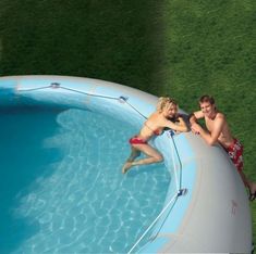 two people are sitting on the edge of a swimming pool and one person is standing in it