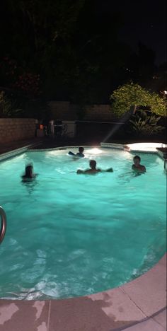 people are swimming in an outdoor pool at night