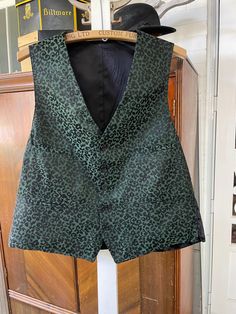 This gorgeous vest is made from a polyester blend in dark green with an overall floral and leaf pattern in black. It has the original buttons, four front pockets and is fully lined. The back is plain black. The measurements, taken with the vest lying flat, are: shoulder to shoulder, 14 1/2 inches; armpit to armpit, 22 inches; front length, 23 inches; bottom edge, 20 inches. In very good condition. Brocade Vest, Green Vest, Vest Waistcoat, Wedding 2024, Black Vest, Vest Outfits, Plain Black, Green And Black, Leaf Pattern