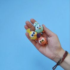 a hand holding three small knitted owls on it's palm against a blue background