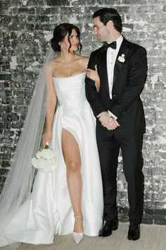 a bride and groom standing next to each other in front of a brick wall