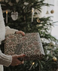 a woman holding a wrapped present in front of a christmas tree