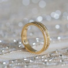 two gold wedding bands sitting on top of each other in front of some silver and white glitter