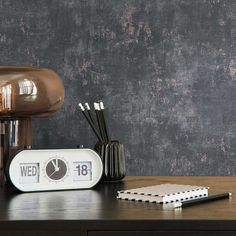 an alarm clock sitting on top of a wooden table next to a pen and notebook