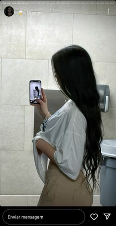 a woman standing in front of a toilet taking a selfie with her cell phone